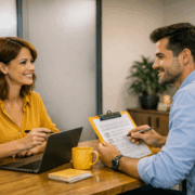Two colleagues seated in a private meeting room conducting a one‑to‑one performance review, with a laptop and clipboard, featuring prominent yellow accents.